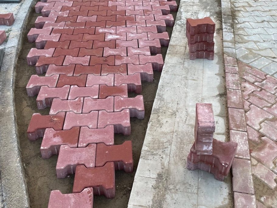 Pflasterarbeiten Rote Pflastersteine sind in einem Muster verlegt, mit einigen Steinen neben dem Weg.